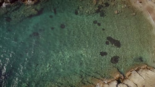 Aerial view of an empty small beach with turquoise water and stones in Greece.