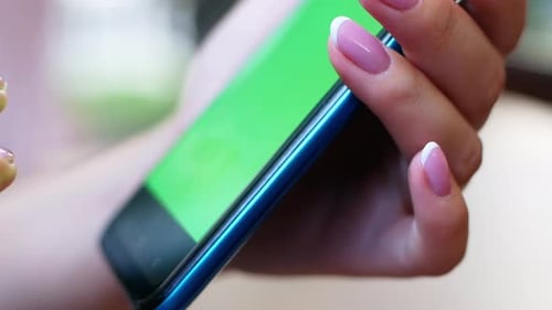 A woman is sitting in a cafe with a smartphone in her hands with a green screen mockup.
