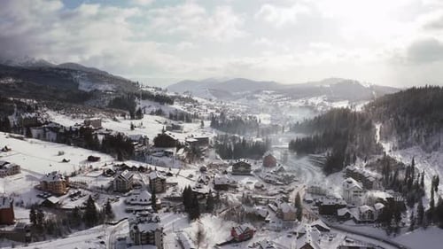 Luftaufnahmen eines kleinen Bergdorfes im Winter bei sonnigem Tag mit epischen Wolken