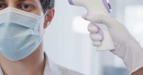 Man wearing face mask getting his temperature measured at office