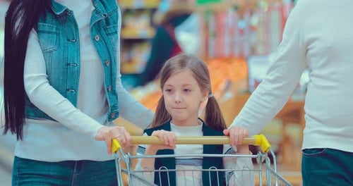 Little Girl Pushes a Shopping Trolley in a Supermarket