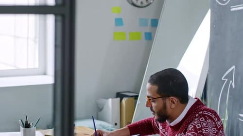 Mann aus dem Nahen Osten tippt auf Laptop und macht sich Notizen am Schreibtisch