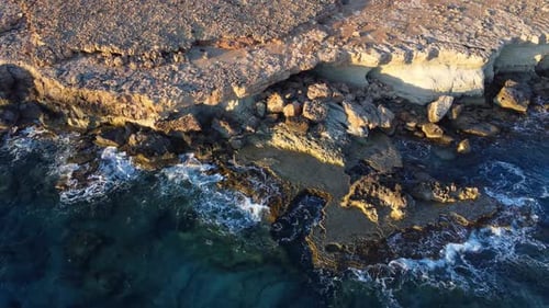 Flying Over Rocky Coastline Alongside Cliffside with Blue Mediterranean Sea Ocean Water Towards the