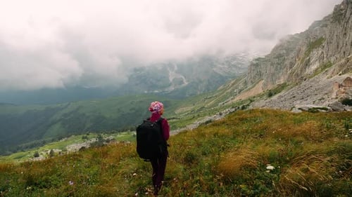 Rear View of Hiking Woman Tourist with Backpack Among Dense Grass on Backdrop of Amazing Caucasian
