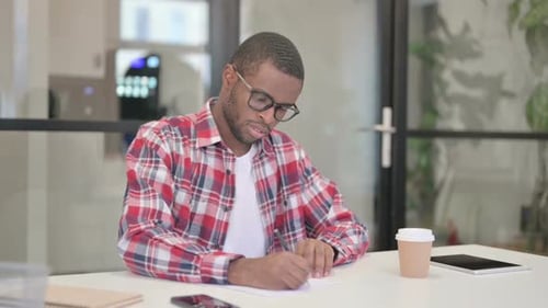 African Man Writing on Paper in Office