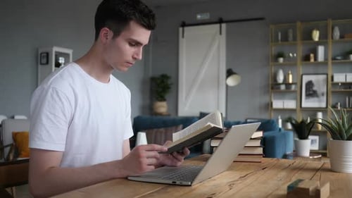 Young Adult Reading a Book and Using Laptop