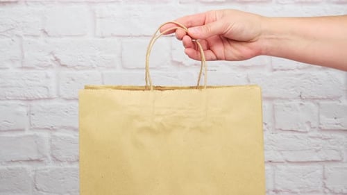 mano femenina pone una bolsa de papel marrón con asas para compras y productos