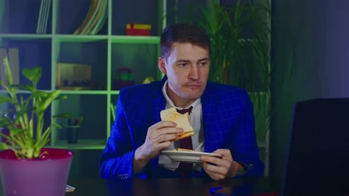 Young Man Eats Sandwich Sitting in Office