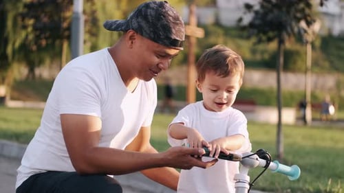 Dad Teaching Son To Drive a Bike in the Summer Park