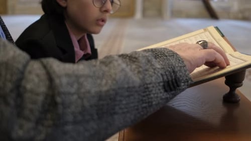 Child Reads Book With Adult in Mosque