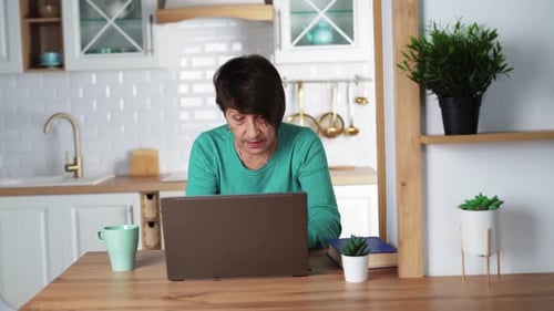 Senior Woman Uses Laptop in Bright Kitchen