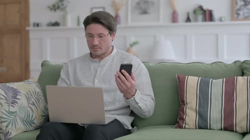 Man Using Laptop and Phone at Home