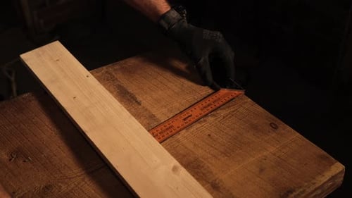Carpenter está dejando una marca en una tabla de madera, preparándose para cortarla en el taller