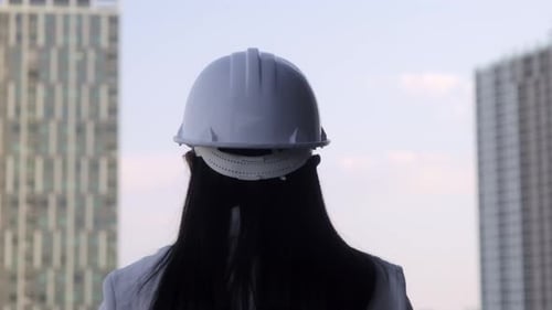 Confident woman architect in white helmet looking at a construction.