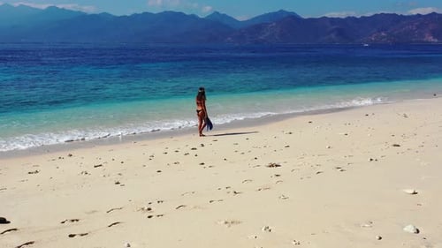 Woman walking through the shallow ocean waves by herself down a beautiful beach shoreline