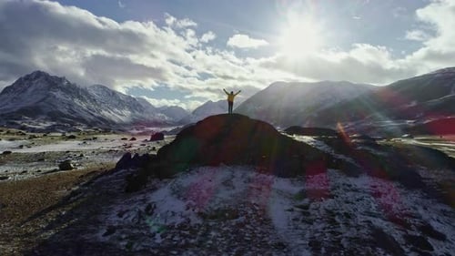 Male mountain climber raising hands with icepick on top of snowy peak. hiker at the top of a rock wi