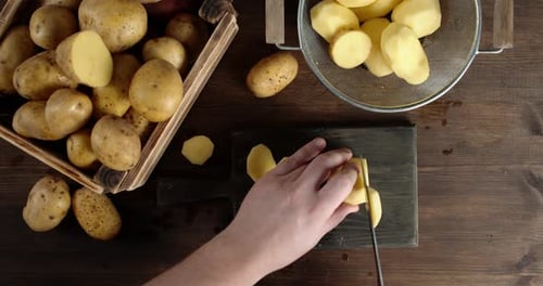 Mãos masculinas cortam batatas frescas em fatias redondas.