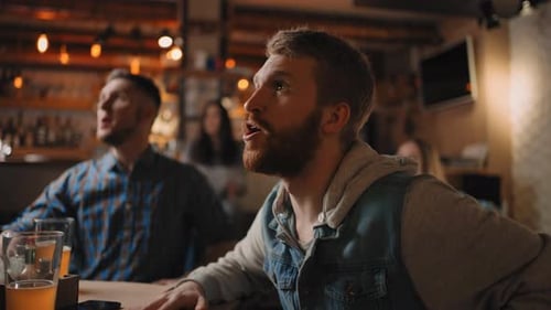 Closeup of a Group of Fans of Men and Women Sitting Together in a Bar and Watching a Broadcast on TV