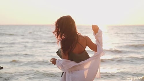 Beautiful Girl Dancing on the Beach in a White Shirt. Free Girl with Long Hair in a White Shirt