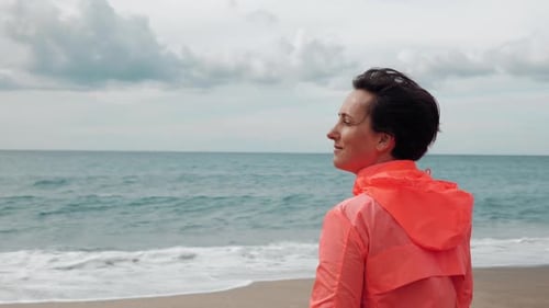 Woman is looking at stormy sea, standing on beach at windy weather