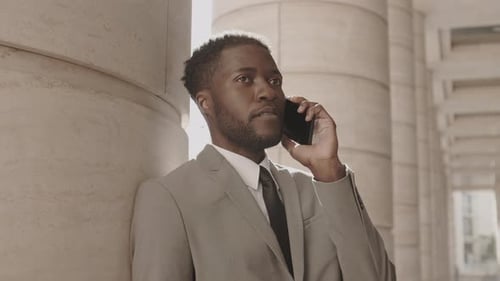 Handsome Businessman Talking on Phone Against Urban Column