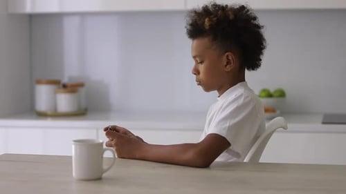Boy Plays Handheld Video Game at Kitchen Table