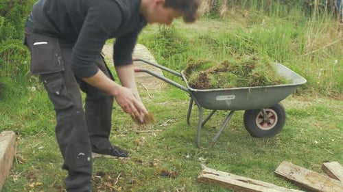 Young Adult Working with Wheelbarrow in Grassy Field