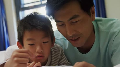 Father and Son Reading Book Together in Bed
