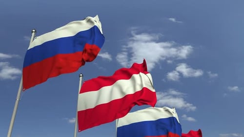 Russian and Austrian Flags Waving in Wind Against Blue Sky