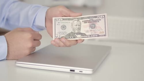 Hands holding fifty dollar bill with laptop