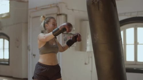 Medium Shot of Exhausted Woman Kicking and Hitting Punching Bag