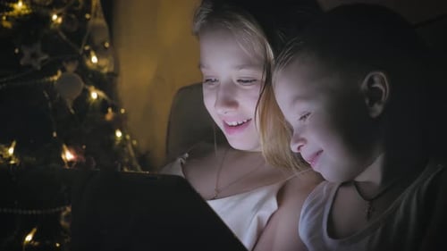 Brother and Sister Watching Tablet Near Christmas Tree