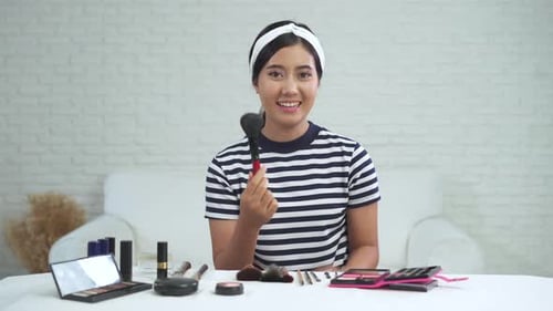 La bloguera de belleza presenta cosméticos de belleza mientras está sentada frente a la cámara frontal para grabar un vídeo.