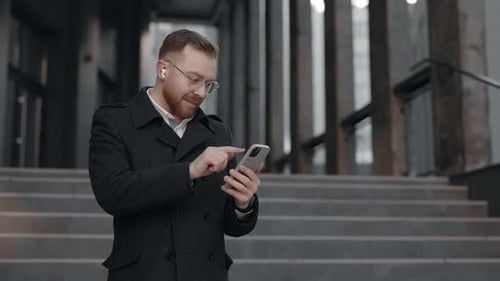 Caucasian Businessman in a Suit is Using a Smartphone Standing Near the Office Building