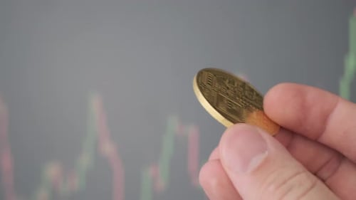 Hand Holding Bitcoin Coin in front of Graph