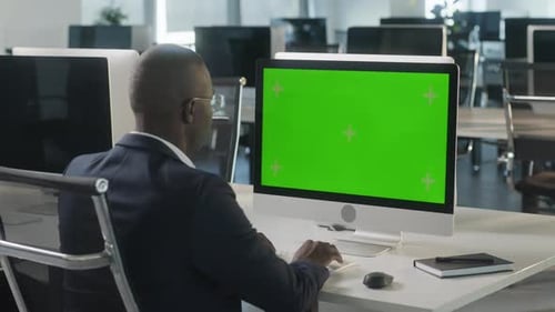 Business AfricanAmerican Man Working on Desktop Computer with Green Screen Mock Up Display in Busy