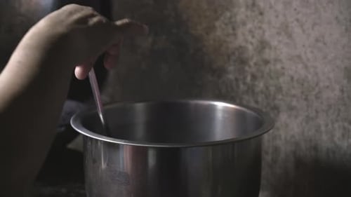 Hand Stirring Food with Spoon in Steaming Pot