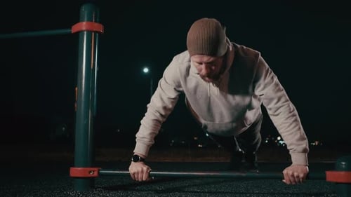 El hombre hace flexiones al aire libre en un área deportiva durante la noche