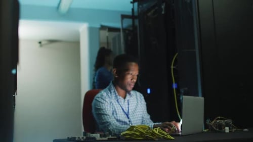 Man Works on Laptop in Server Room