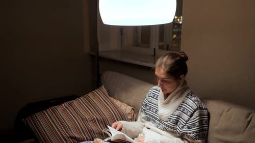 Woman Reading Book on Sofa at Night