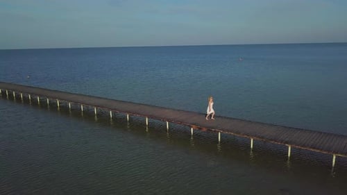 A Girl Walks on a Wooden Pier Near the Sea