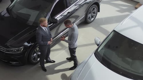 Salesman Giving Car Key and Handshake to Customer in Auto Showroom