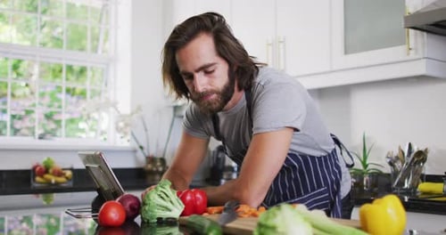 Man Reads Tablet While Preparing Vegetables in Kitchen