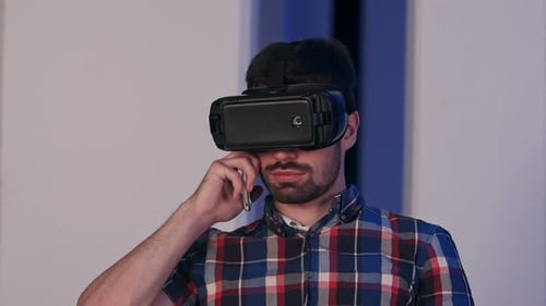 Ernsthafter junger Mann mit Virtual-Reality-Brille telefoniert
