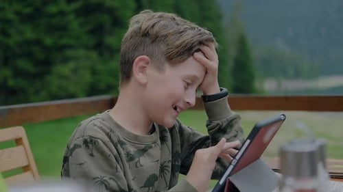 Netter aufgeregter Junge spielt mit dem Tablet, während er draußen sitzt.