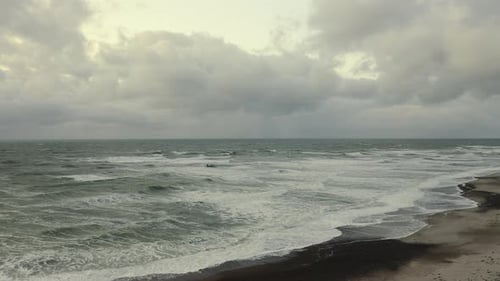 Cloudy Skies and Waves Crashing Against the Shallow Depths of the Beach Coast