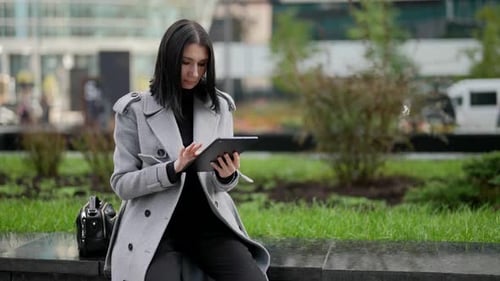Businesswoman is Sitting on Street in Downtown and Working with Tablet