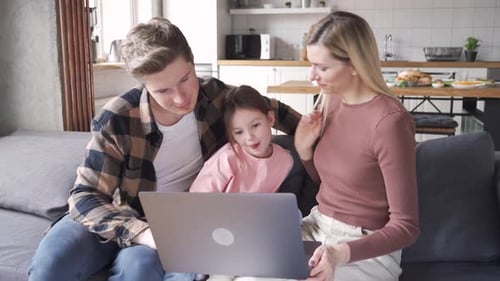 Happy Young Parents and Kid Child Daughter Using Laptop Sit on Couch at Home