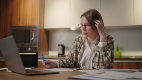 A Woman Works Remotely From Home Sitting at a Table with a Laptop and a Felttip Pen Marks the Data