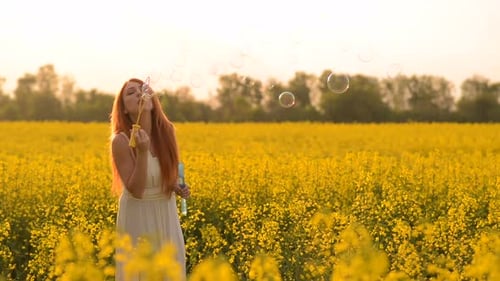 Young Redhair Woman Blowing Bubbles at the Camera Outdoors in Summer Meadow